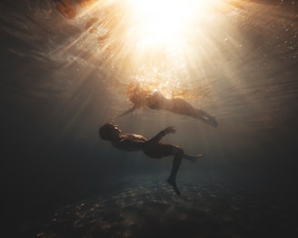 A diver gently holding hands with an instructor underwater, surrounded by soft natural light.