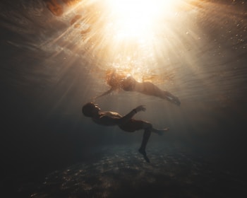 An underwater shot of a couple embracing, surrounded by clear blue water and sunlight beams.