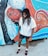 A person with dreadlocks, wearing a white shirt, dark shorts, and sunglasses stands in front of a vibrant mural. The mural depicts a stylized female figure with intricate details and a rich color palette, including elements of an octopus with swirling tentacles.