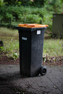 Close-up of a sanitized trash bin lid with water droplets glistening, set against a blurred suburban lawn.