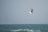 A person is engaged in kitesurfing, skillfully maneuvering high above the ocean waves. They are holding onto a kite that provides lift and control as they soar through the air. The ocean beneath them appears rough with small waves, and the sky is a plain light blue color.