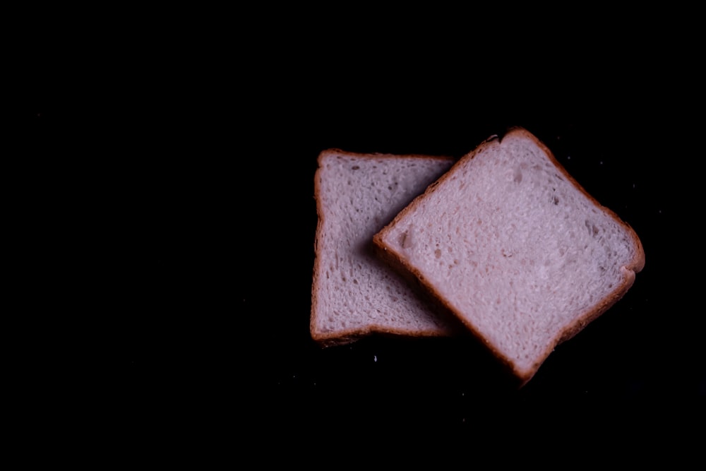 dois pedaços de pão sentados em cima de uma superfície preta