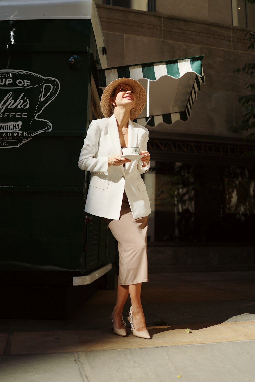 a woman in a white suit and hat standing in front of a coffee truck