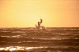 Sunset silhouette of an efoil rider flying above the water, casting golden reflections on the sea.