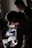 Two individuals are focused on examining various papers and items on a cluttered desk. The lighting is dim, casting shadows across the scene while illuminating the papers being handled. The atmosphere suggests a sense of concentration and attention to detail.