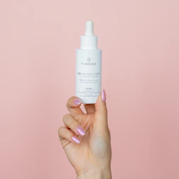 Elegant applicator bottle dispensing nourishing oil onto fingertips.
