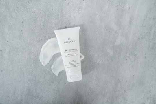A tube of bio hand cream with the brand name Plantagea is placed on a textured gray surface. The cream has been squeezed out next to the tube, forming a swirl pattern.