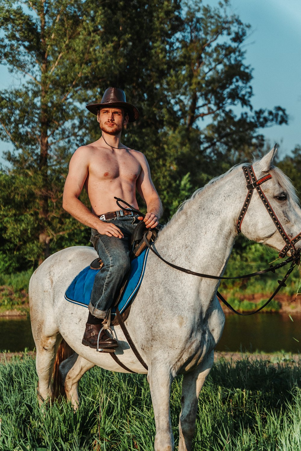 a shirtless man riding a white horse in a field