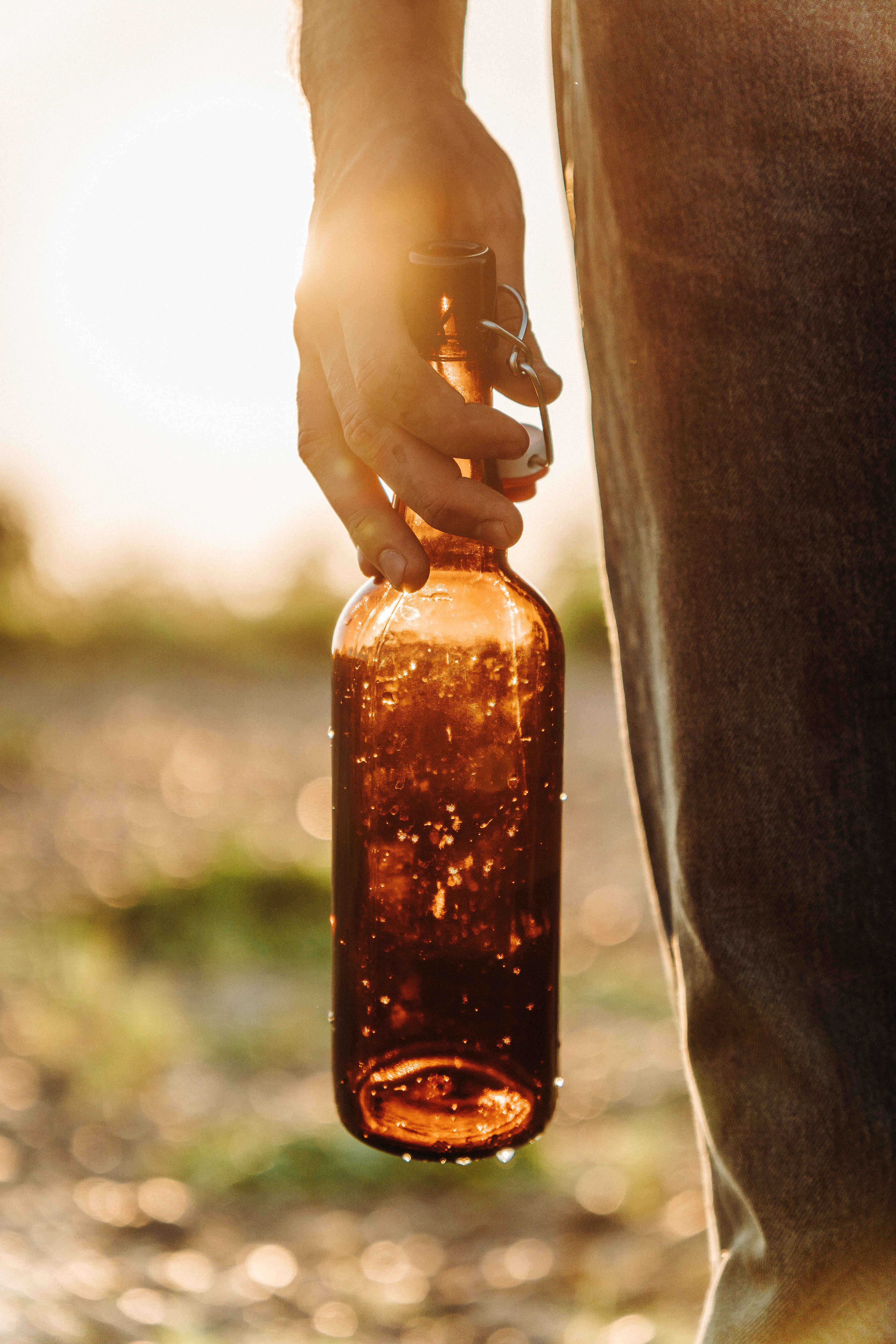 Hand holding an amber glass bottle against golden backlight in a field