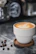 A steaming cup of coffee beside elegant coffee equipment with a backdrop of Penang skyline.