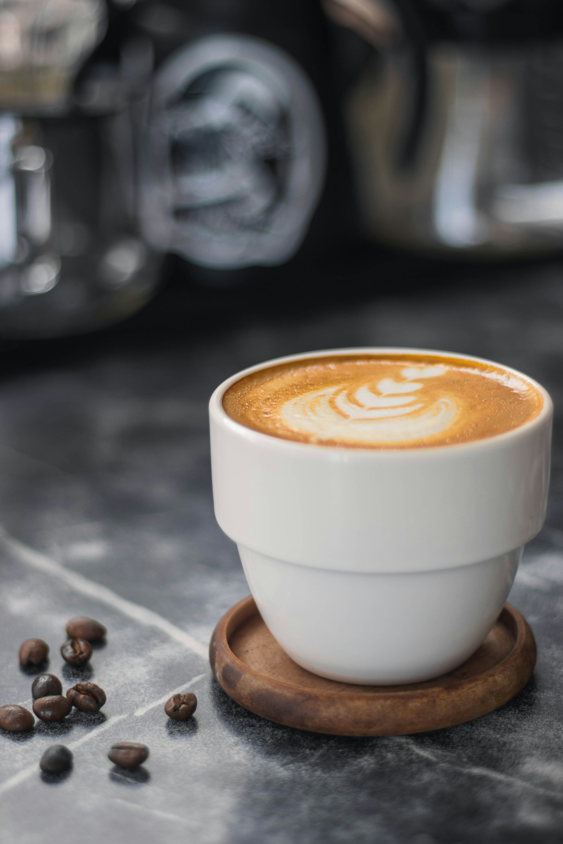 A steaming cup of artisan coffee placed on a rustic countertop, with a blurred background of coffee brewing equipment.