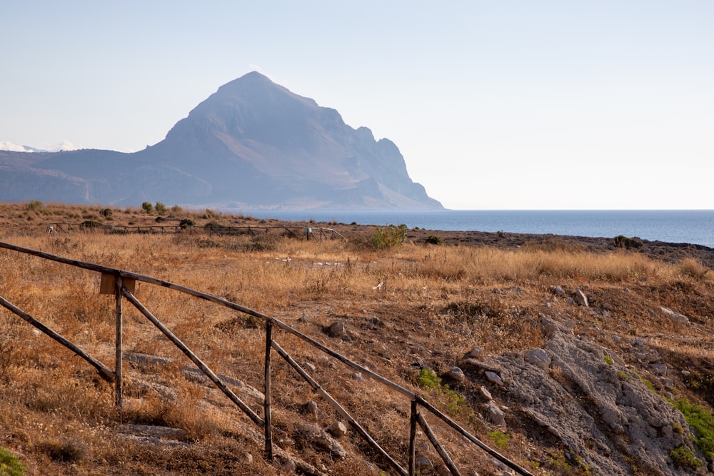 a wooden fence in a field with a mountain in the background