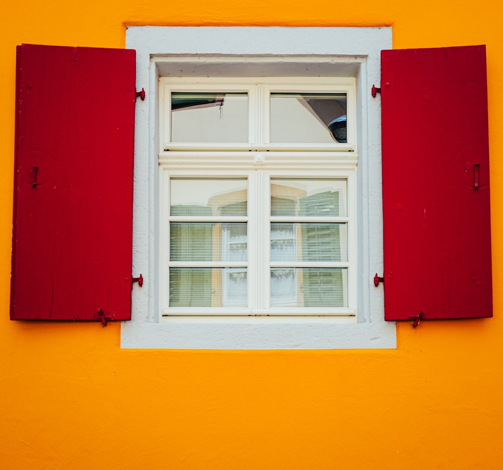 a window with red shutters on a yellow wall