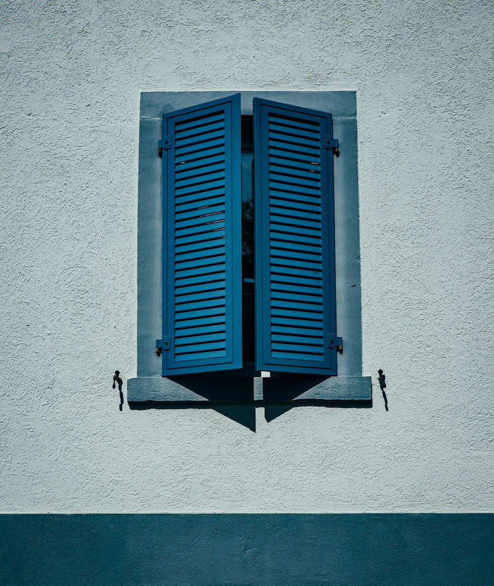 a window with blue shutters on a white wall