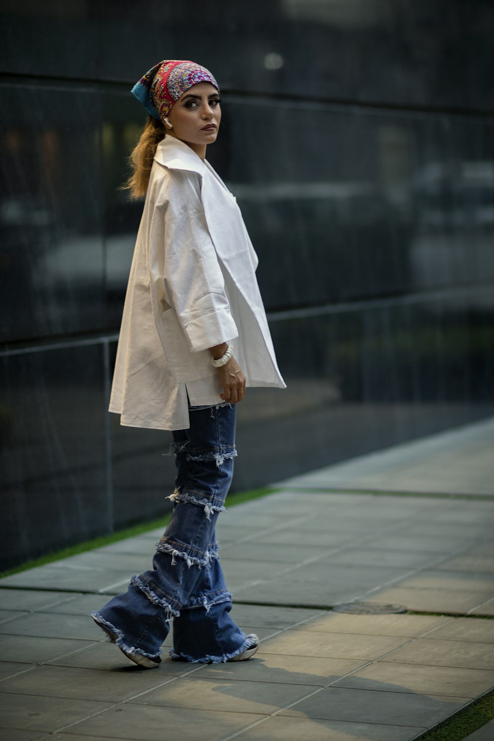 a woman is walking down the sidewalk in a white coat