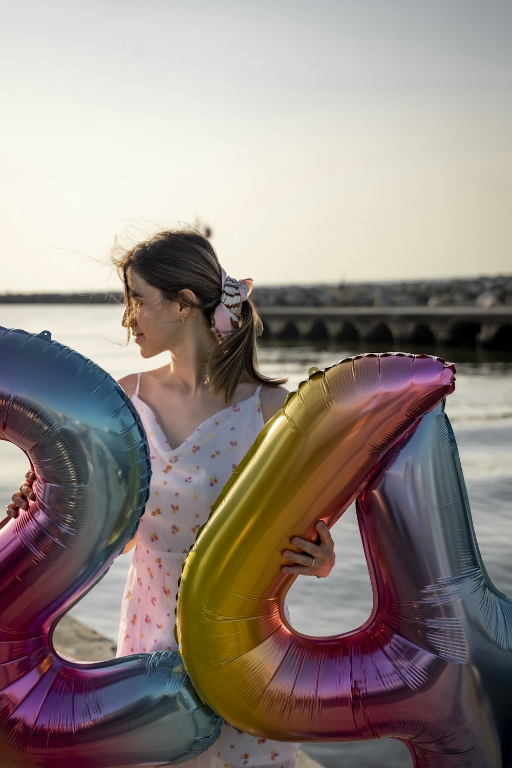 a woman holding a large number balloon in front of a body of water