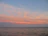 A serene view of the guesthouse balcony overlooking the calm ocean at sunset, with warm pastel skies.