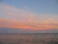 A serene view of the guesthouse balcony overlooking the calm ocean at sunset, with warm pastel skies.