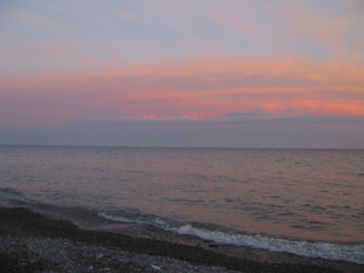 A small square image of a calm beach with gentle waves and a pastel sunset.