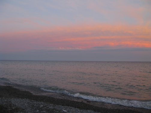 A small square image of a calm beach with gentle waves and a pastel sunset.