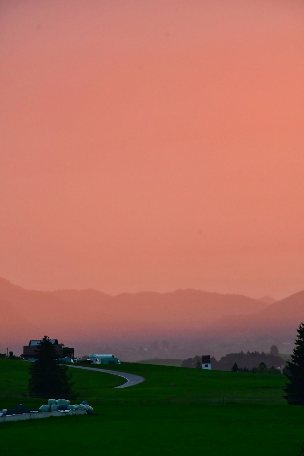 a red sky over a green field with a road in the foreground