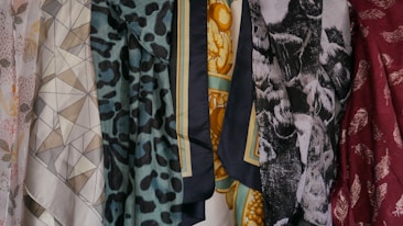 A collection of patterned and colorful fabrics is displayed, featuring geometric shapes, floral patterns, animal prints, and abstract designs. There are six distinct pieces of fabric shown, each with its own unique print and color palette.