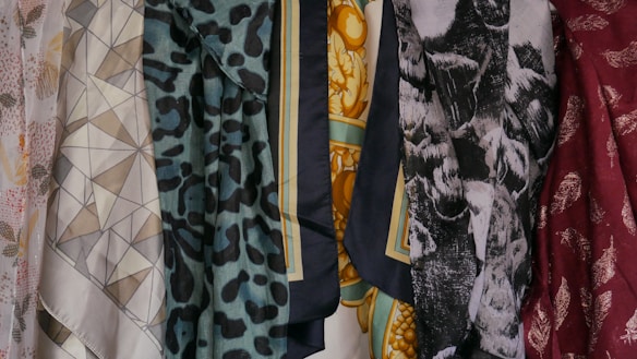 A collection of patterned and colorful fabrics is displayed, featuring geometric shapes, floral patterns, animal prints, and abstract designs. There are six distinct pieces of fabric shown, each with its own unique print and color palette.