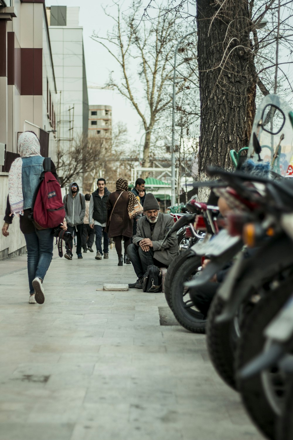 a group of people walking down a sidewalk next to parked motorcycles