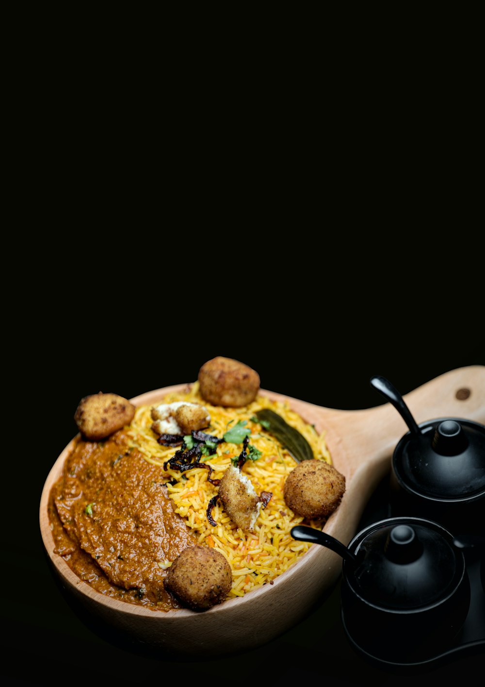 a wooden bowl filled with food next to two black cups