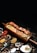 A wooden platter holding skewered grilled meat, surrounded by various colorful spices and herbs. The presentation includes a mix of textures with creamy sauces and vibrant garnishes.