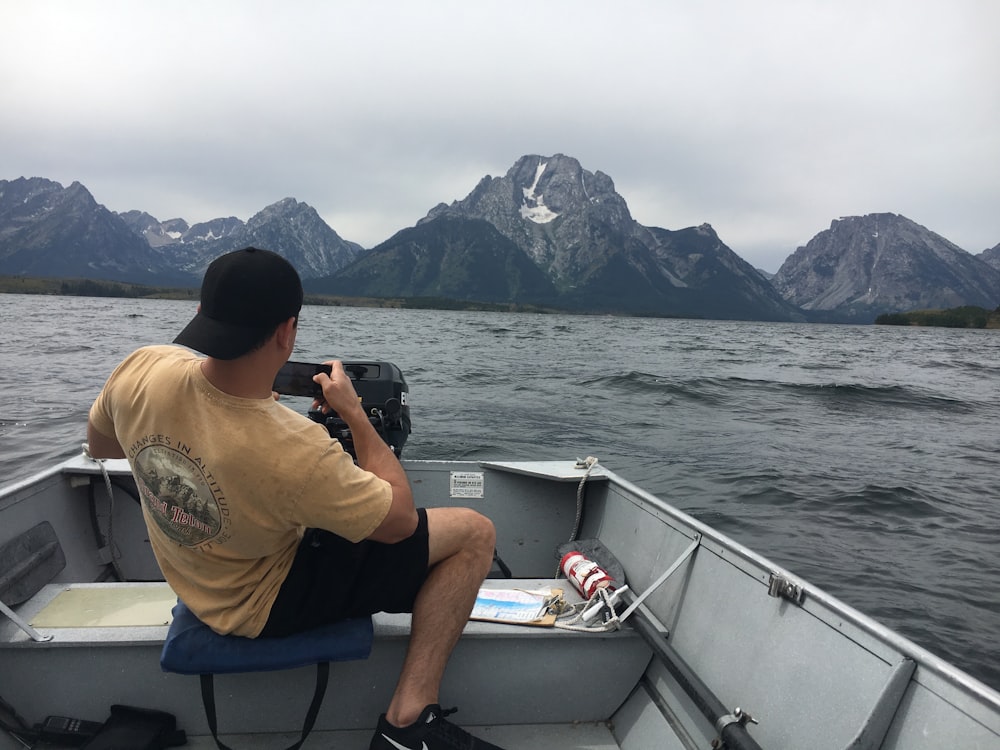 a man sitting in a boat taking a picture of mountains