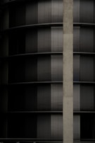 A building facade with a series of dark horizontal blinds alternating between closed and partially open positions. A vertical concrete column runs along the right side of the image.