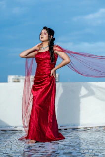 A flowing ruby red chiffon gown catching the breeze against an urban backdrop.