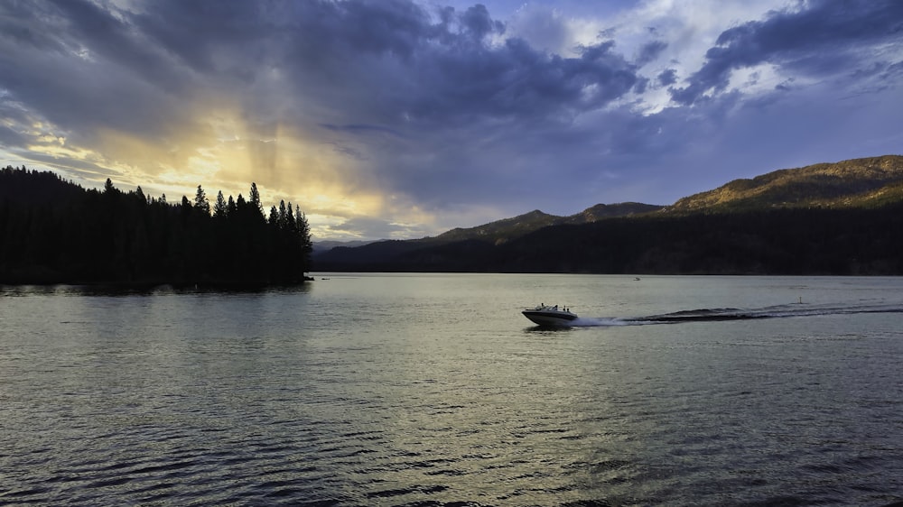 a boat traveling across a lake under a cloudy sky