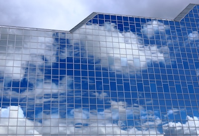 Reflective glass windows of a modern building mirror the blue sky and clouds, creating a pattern of rectangular panes that enhance the architectural aesthetics.