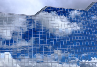 Reflective glass windows of a modern building mirror the blue sky and clouds, creating a pattern of rectangular panes that enhance the architectural aesthetics.