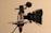 A professional video camera setup is mounted on a tripod. The camera features a matte box, a shotgun microphone with a windscreen, and a side grip with a wood finish. The equipment is composed of multiple intricate components highlighting its advanced functionality and design.