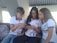 Three young people wearing casual school uniforms are sitting together, engaged with a smartphone. The individuals appear to be sharing something interesting on the phone, and they seem to be in a bright, indoor setting.