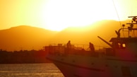 Sunset silhouette of a boat speeding across the water with mountains in the background.