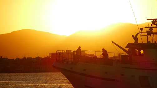 Sunset view from the boat deck with silhouettes of travelers and vast ocean horizon.