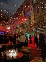 Happy guests at a backyard party chatting near the luxury RV bathroom under string lights at dusk.