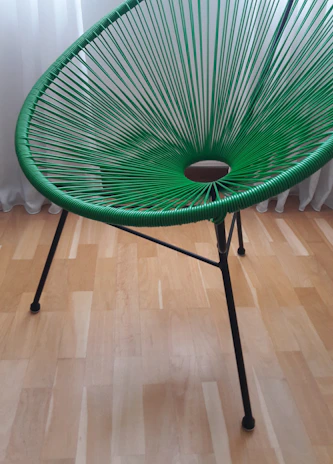 Close-up of a sleek olive green wooden chair with black metal legs in a bright, minimalist room.