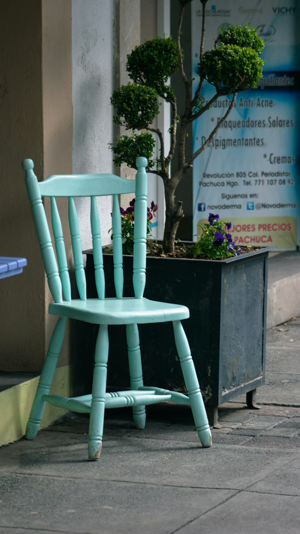 a blue chair sitting on a sidewalk next to a potted plant