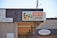 A sign for a coin-operated laundry is prominently displayed, featuring an illustration of a person doing laundry. Next to it is a sign for a tattoo shop named Rollin Gypsy Tattoo. Various payment methods accepted are shown on another sign, including EBT and major credit cards. An overhang and a satellite dish are visible on the building's roof.