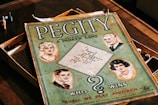 A vintage board game box with the title 'Pegity' prominently displayed. It features illustrations of four people, two men and two women, set in a retro style. The board inside the box is visible along with colored pegs. The phrase 'Who Wins' and 'Shall We Play Another' are included on the cover.
