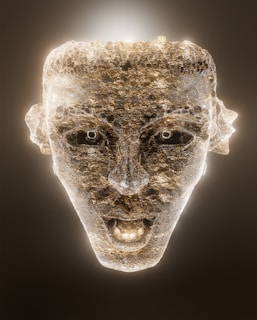 A glowing, textured sculpture of a human face made of stone with a luminous outline and bright facial features against a dark background. The mouth is slightly open, providing a dramatic, ethereal appearance.