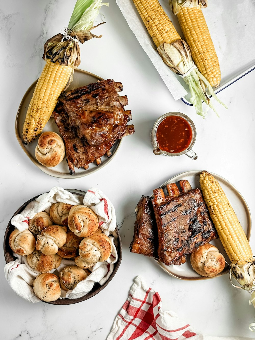A spread of ribs, corn, rolls, and sauce set out for a group