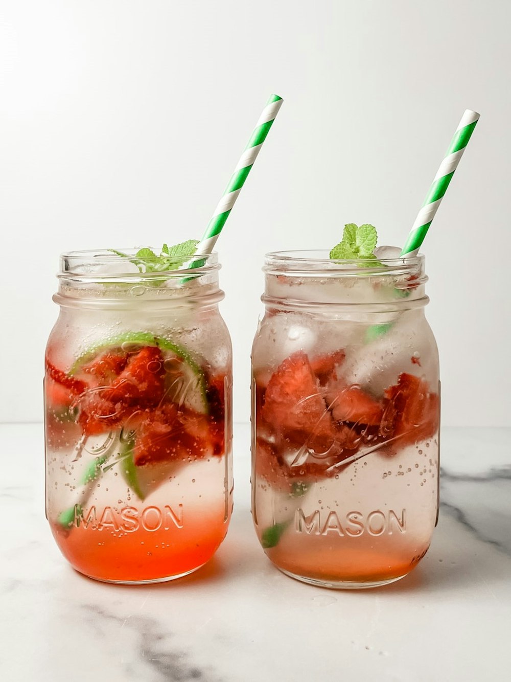 two mason jars with strawberries and mint on a marble table