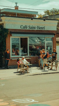 A bustling local cafe with new customers enjoying outdoor seating on a sunny day.