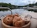 A wooden tray is topped with several sesame seed bagels alongside a couple of plastic containers filled with spreads or salads. In the background, there is a tranquil view of a lake with boats docked near the shoreline, surrounded by lush greenery and a cloudy sky.
